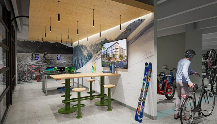 Interior view of the "Colorado Room" at Tempo Nine Mile Station in Aurora, Colo., featuring a modern lounge area with high-top tables, a mural of mountain scenery, and a TV. The space includes bike racks, ski and snowboard storage, and a gear repair station, catering to residents with an active outdoor lifestyle.