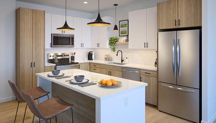 Modern kitchen at Tempo Nine Mile Station in Aurora, Colo., featuring a sleek island with seating, stainless steel appliances, quartz countertops, wood-grain cabinetry, and pendant lighting. The stylish and functional space is designed with contemporary finishes and an open-concept layout.