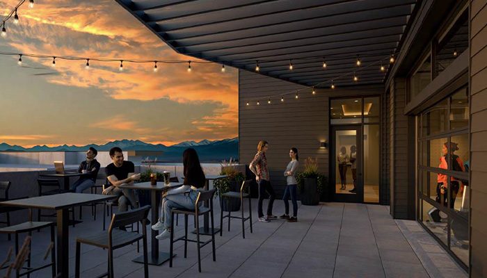 Rooftop deck at Tempo Nine Mile Station in Aurora, Colo., featuring outdoor seating, string lights, and stunning mountain views at sunset. Residents are seen enjoying drinks, socializing, and taking in the scenic backdrop in this stylish and inviting communal space.