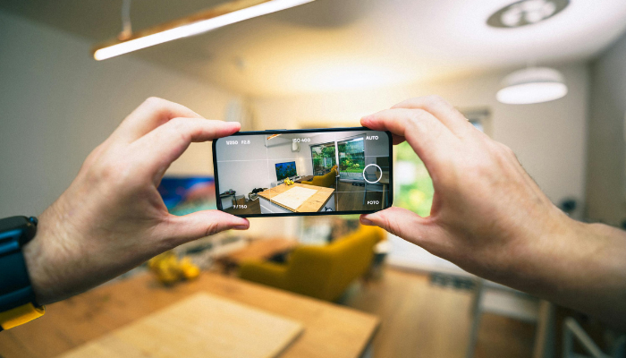 A person holding a smartphone and taking a photo of a modern, well-lit apartment interior, capturing the space for reference.