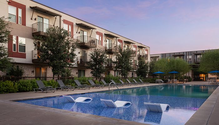 Exterior view of Senita on Cave Creek, a luxury apartment community in Phoenix, featuring a resort-style pool with lounge chairs, surrounded by lush greenery and modern apartment buildings.