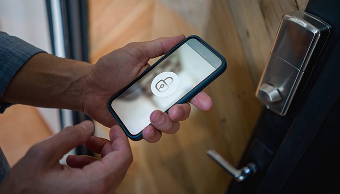 A person using a smartphone to unlock a smart door lock, illustrating the role of AI-driven automation in modern multifamily security and resident convenience.