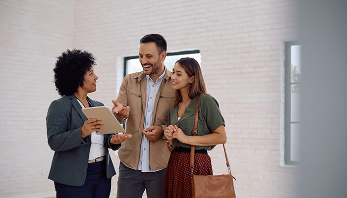 A leasing agent using a tablet to discuss apartment options with a smiling couple during a property tour, representing AI-driven leasing and modern multifamily experiences.