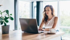 Woman sitting at a kitchen counter using a laptop, researching apartments and protecting personal information online.