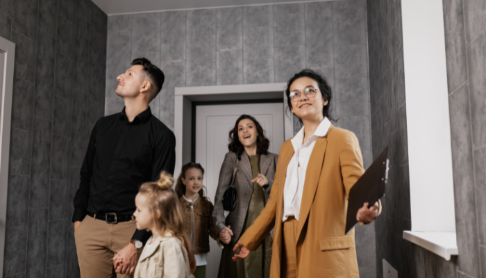 A family tours an apartment with a real estate agent, exploring the hallway. The agent holds a clipboard while the family looks around with interest, assessing the space.