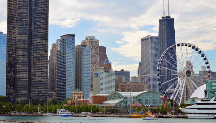 View of the Chicago skyline from Navy Pier, featuring the Centennial Wheel, skyscrapers, and boats along Lake Michigan under a partly cloudy sky.