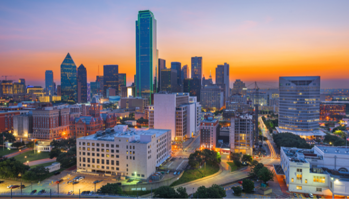 Skyline of downtown Dallas, Texas at sunset with modern high-rises, historic red-brick buildings, and city lights beginning to glow — a visual snapshot of the vibrant and rapidly growing Dallas/Fort Worth metroplex.
