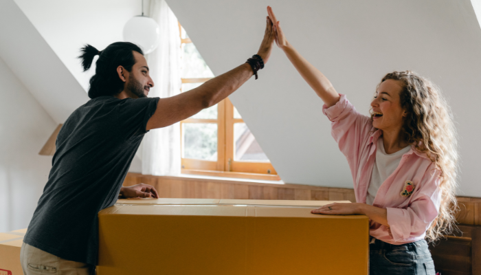 A smiling couple gives each other a high-five while unpacking boxes in their new apartment.