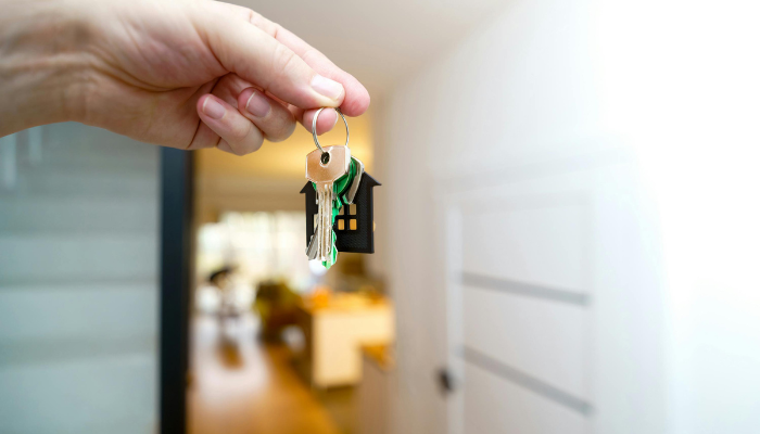 A hand holding a keychain shaped like a house with several keys, symbolizing moving into a new apartment.