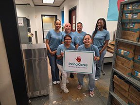 Group of Draper and Kramer employees wearing blue volunteer shirts posing inside a pantry room, with one person holding a sign that reads ‘Irving Cares.’