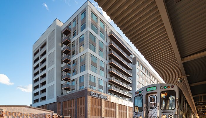 Exterior view of Eleven33 Apartments in Oak Park with CTA train at nearby station, showcasing modern architecture and transit access.