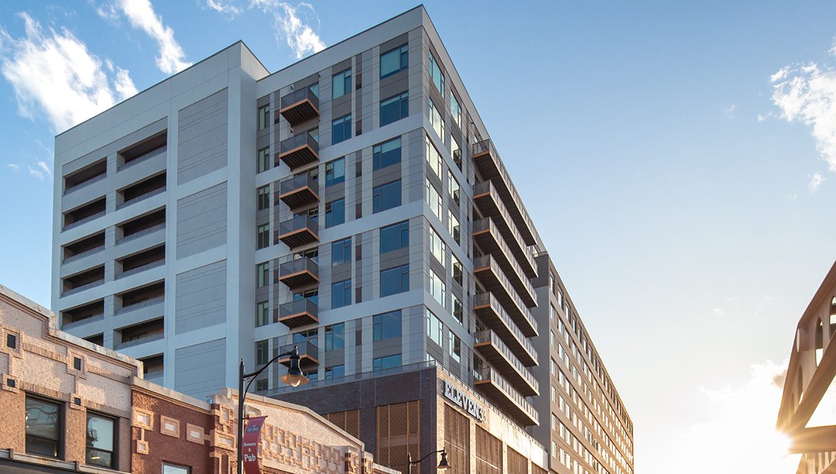 Street view of Eleven33 Apartments in downtown Oak Park with nearby restaurants, shops, and CTA station under evening light.