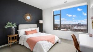 Modern bedroom at Eleven33 Apartments in Oak Park featuring dark accent wall, large window with skyline view, and contemporary decor.