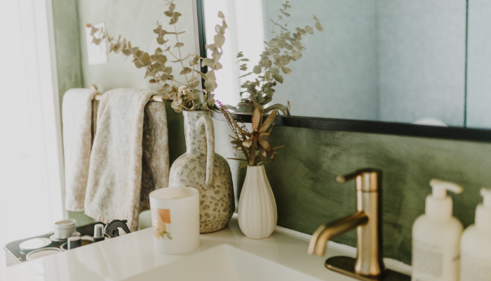 Bathroom vanity styled with neutral towels, ceramic vases, eucalyptus stems, and a brass faucet for a calm, spa-like feel.