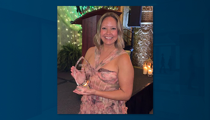 Kelli Stuart stands smiling in a floral gown while holding the 2026 CPM Excellence Award trophy at IREM Chicago’s Premier Awards event at the Drake Hotel in Chicago.