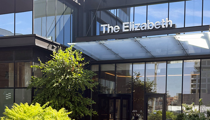 The Elizabeth apartment tower entrance at 225 N. Elizabeth St. in Chicago’s Fulton Market, featuring a glass façade, covered entry and landscaped greenery.