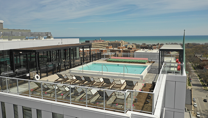 Rooftop swimming pool at Eva in downtown Evanston, featuring lounge chairs, glass railings, and panoramic views of the surrounding city and Lake Michigan.